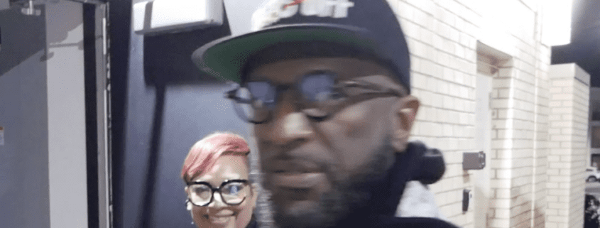 Two people smiling indoors, wearing glasses.